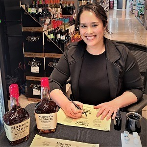 Melissa sitting at a table with Maker's Mark Whisky bottles during a live on-site calligraphy event