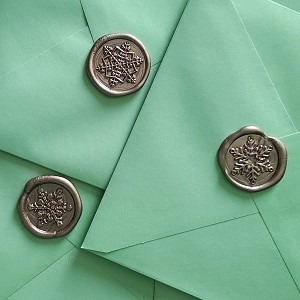 A pile of green envelopes sealed with snowflake wax seals