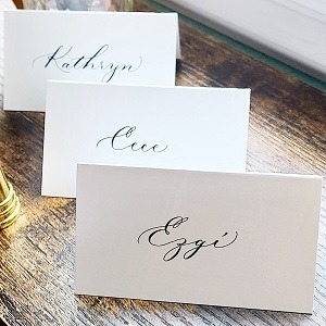 Three white, tented placed cards with names written in modern calligraphy for a wedding rehearsal party